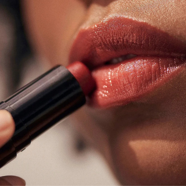 Close-up of a person applying red lipstick to their lips.