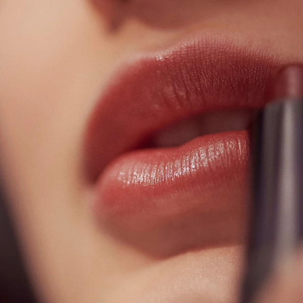 Close-up of a person applying pink lipstick with a brush.