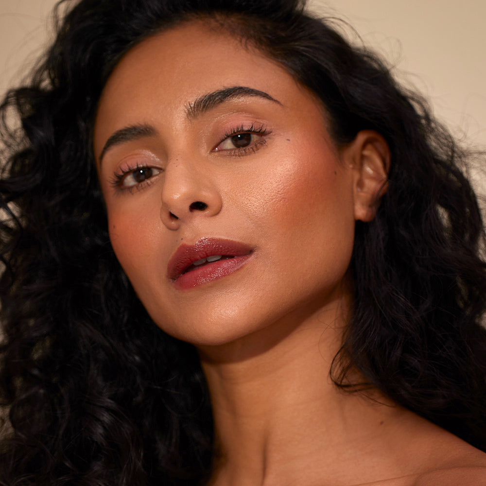 Close-up of a woman with dark hair and makeup on a neutral background