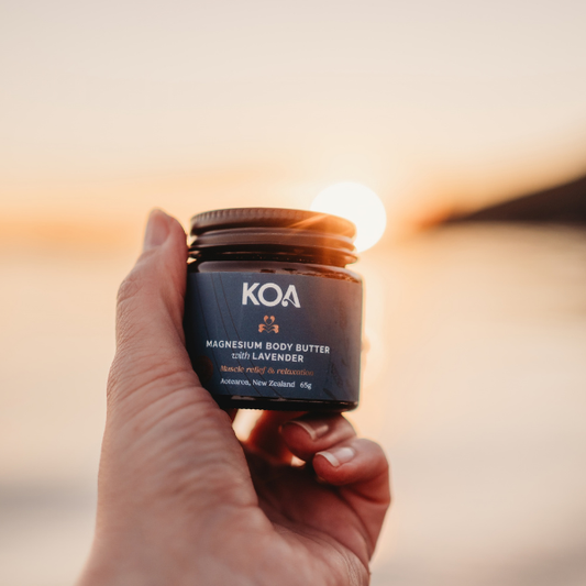 Hand holding a jar of KOA magnesium body butter with a sunset in the background