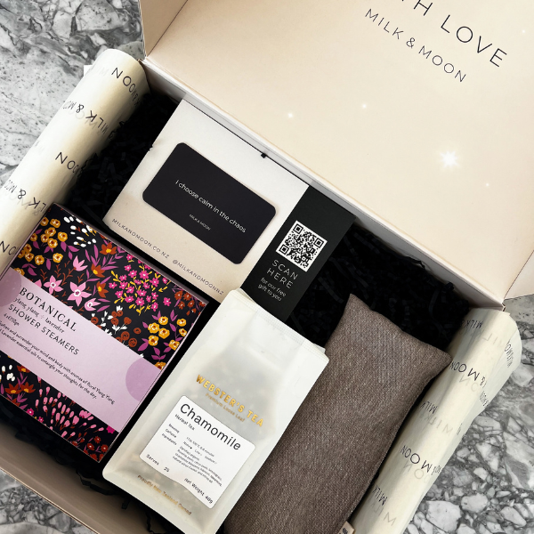 Gift set with botanical shower steamers, towel, and other items from Milk & Moon on a marble surface.