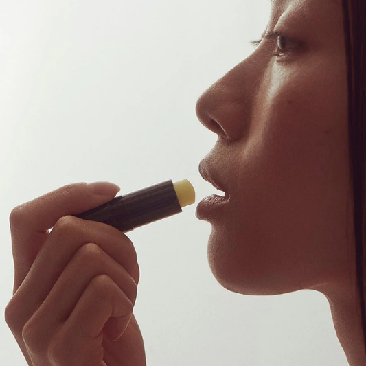 Person applying lip balm to their lips with a neutral background