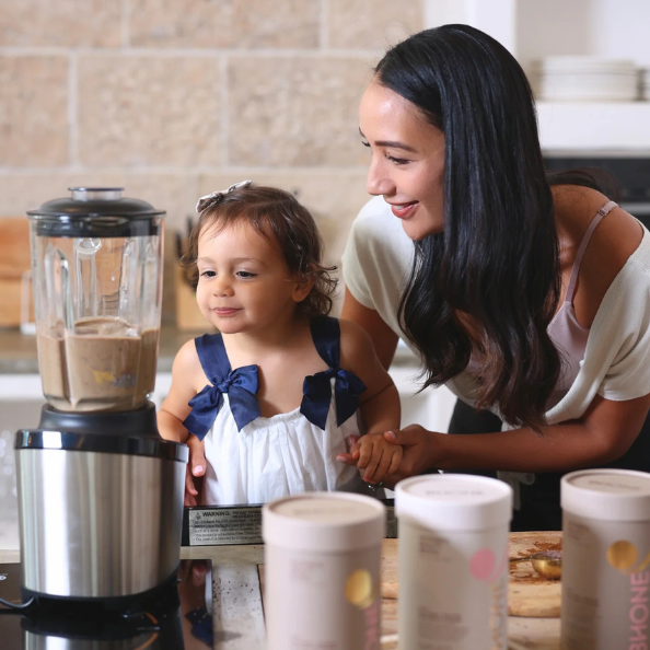 Woman and child in a kitchen with a blender and containers on the counter.