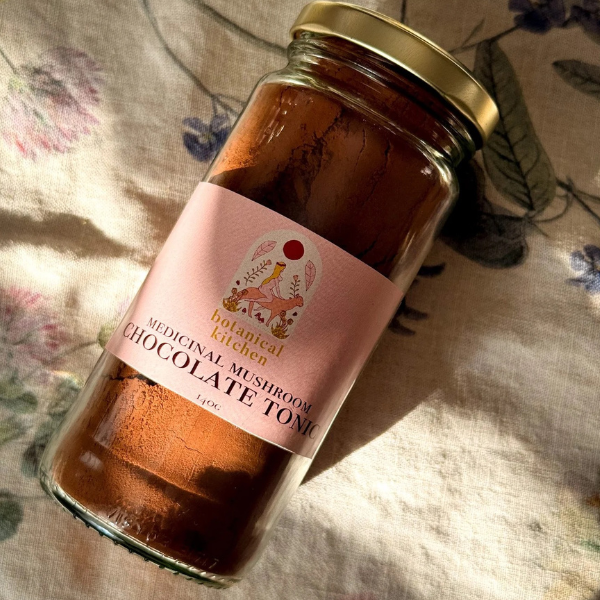 Jar of medicinal mushroom chocolate tonic with a pink label on a floral fabric background